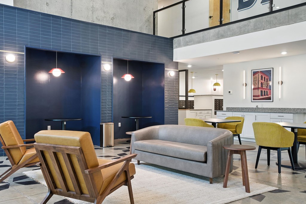 A modern living room with a grey couch, yellow chairs and a blue tiled wall.