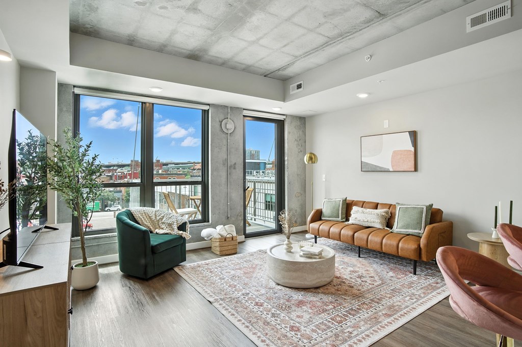A living room with a green chair, a brown couch, and a large window with a view of the city.