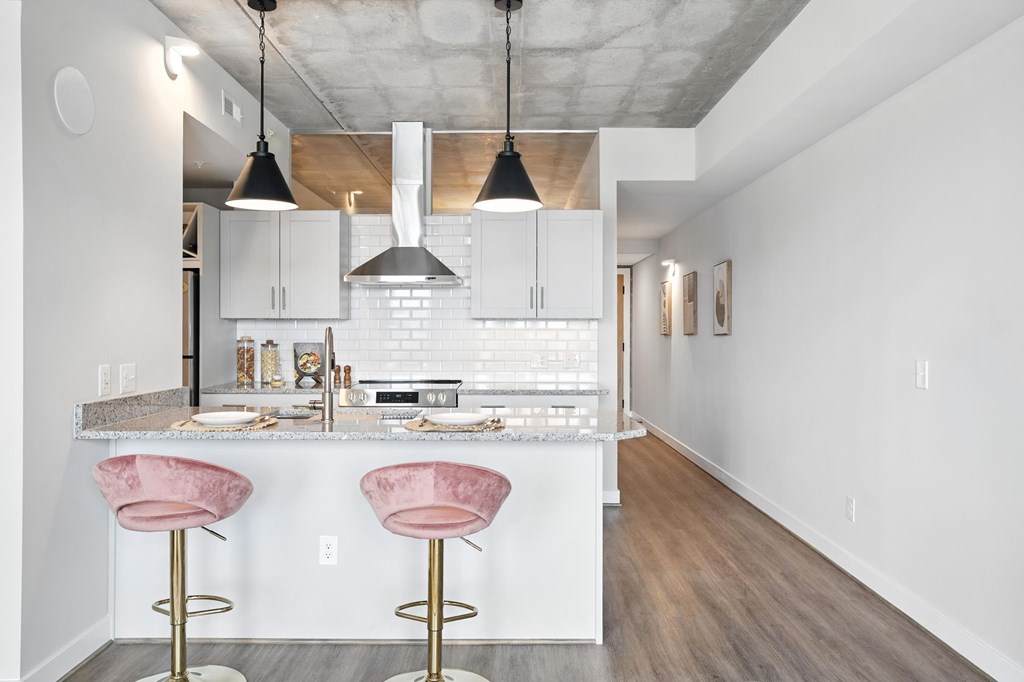 A kitchen with a white counter and pink bar stools.