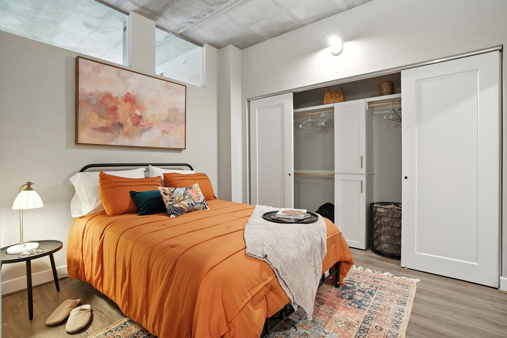 A bedroom with an orange bedspread and a painting on the wall.