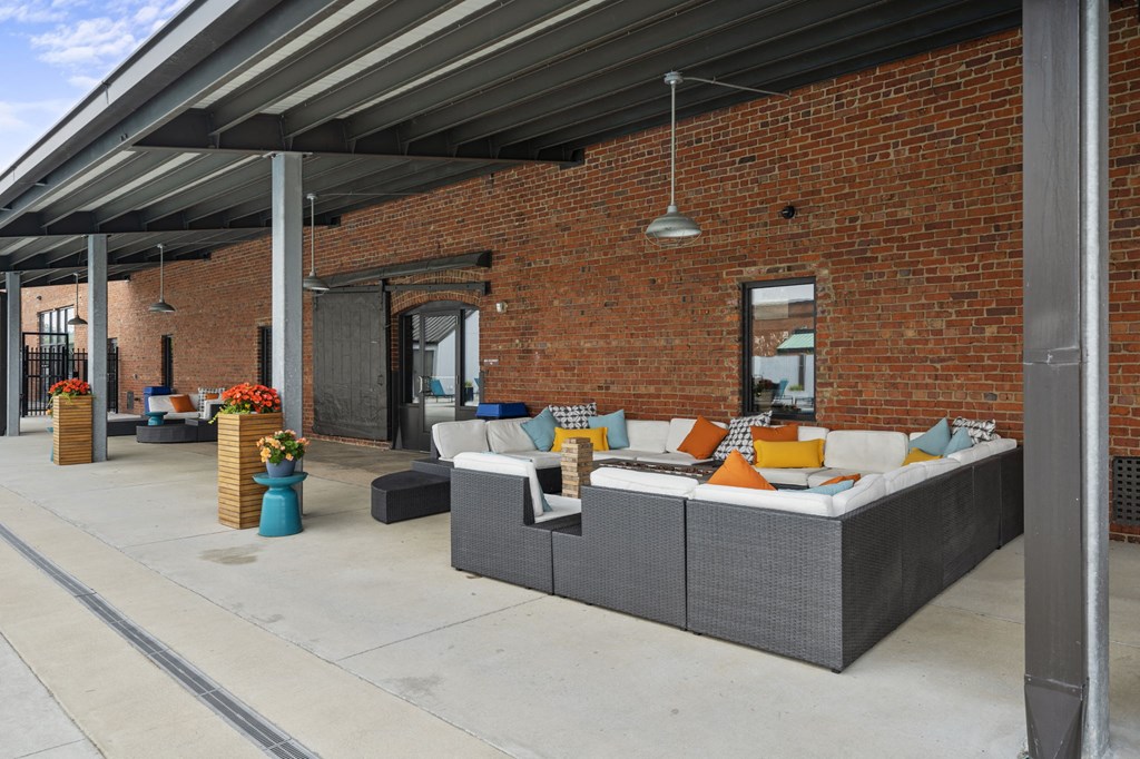 a patio with couches and colorful pillows in front of a brick building