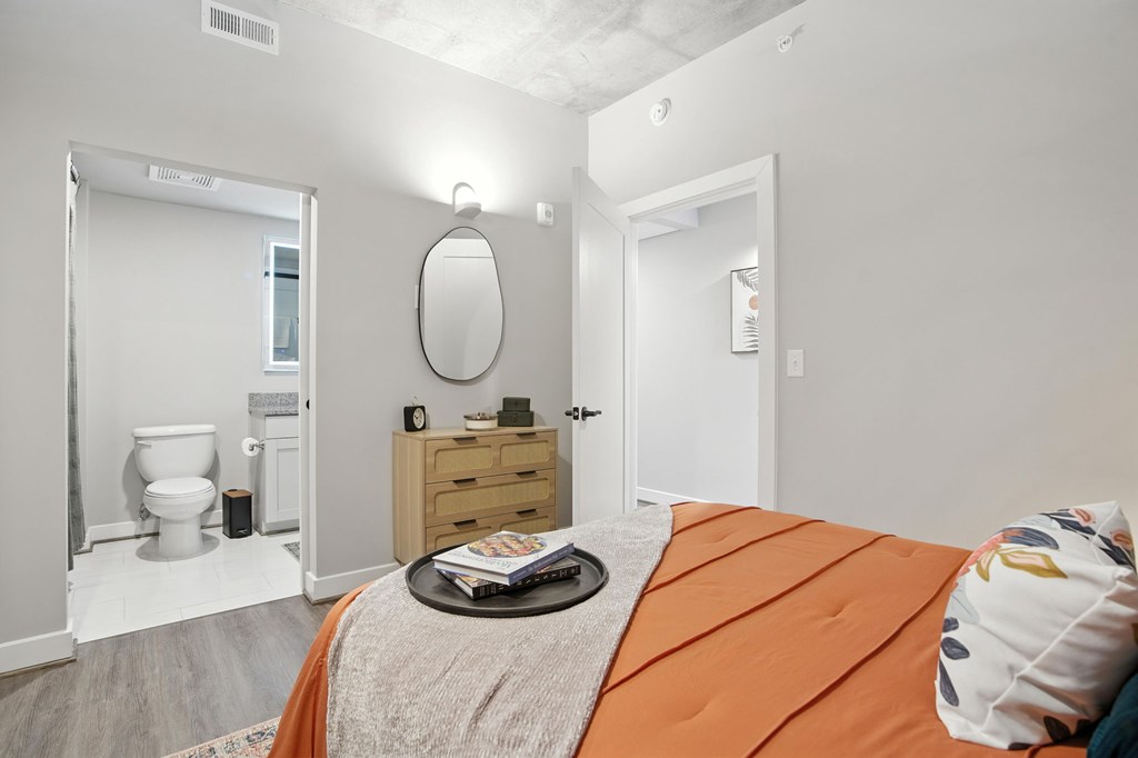 A bedroom with a bed, dresser, mirror, and toilet.