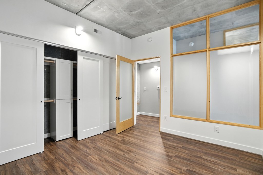 A room with white walls and wooden floors has a glass partition wall and a white door.