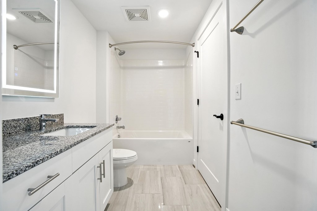 A white bathroom with a granite counter top and a walk-in shower.