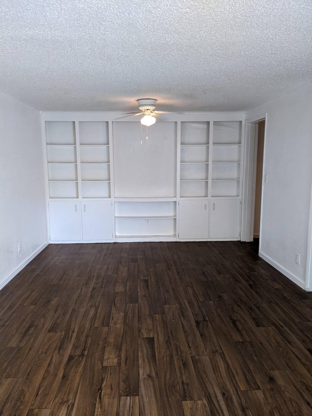 an empty living room with a wood floor and white shelves