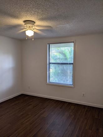 an empty living room with a ceiling fan and a window