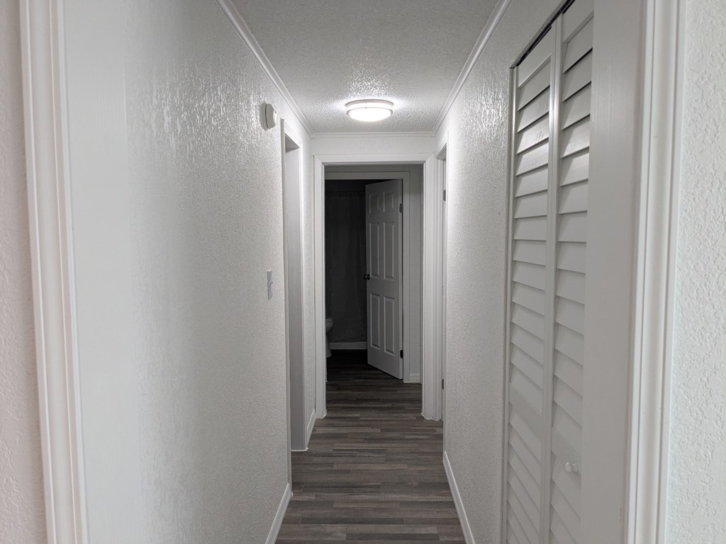 A long, narrow hallway with white walls and a wooden floor.