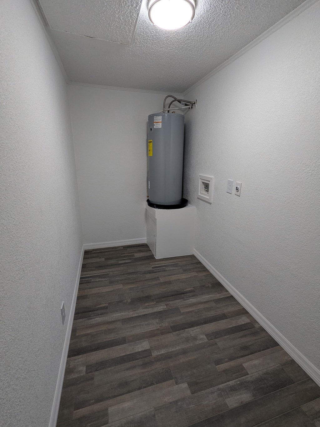 A room with a grey floor and a grey water heater on the wall.