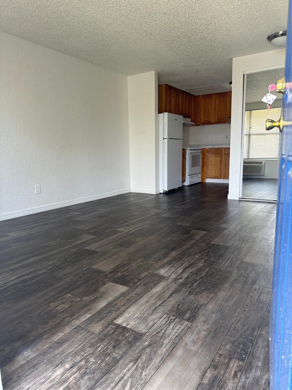 an empty living room with wood floors and a kitchen