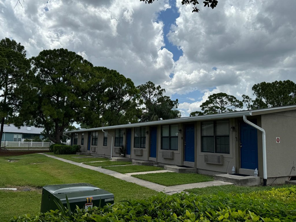 an empty motel building with blue doors and a grass field