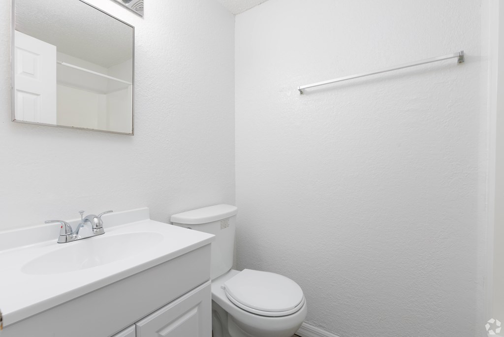 A white bathroom with a toilet, sink, mirror, and towel bar.
