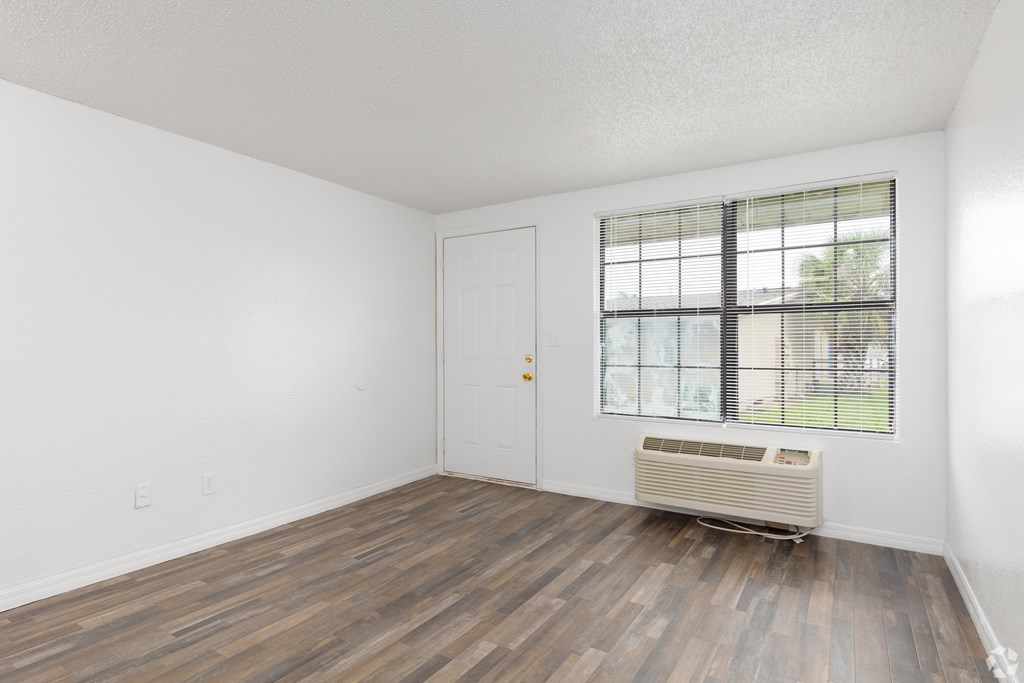A room with a wooden floor and a window with blinds.