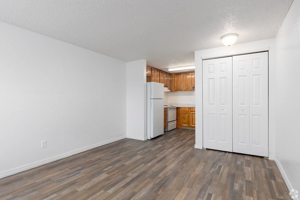 A room with a white door and a kitchen in the background.