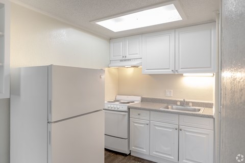 A white kitchen with a refrigerator, sink, and cabinets.