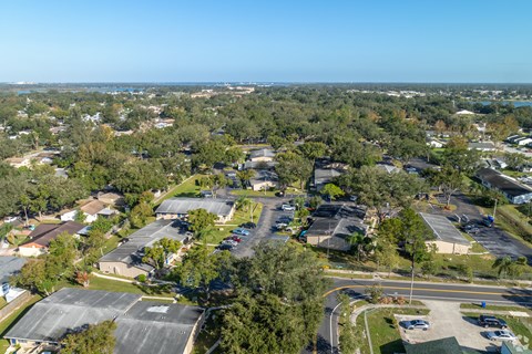 A bird's eye view of a suburban area with houses, trees, and a parking lot.