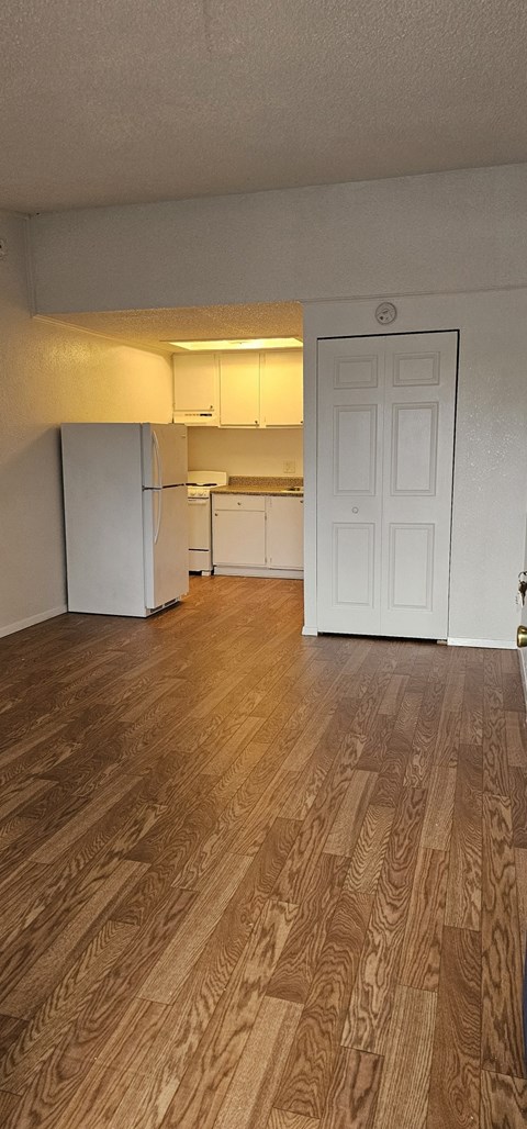 an empty living room with a refrigerator and a door