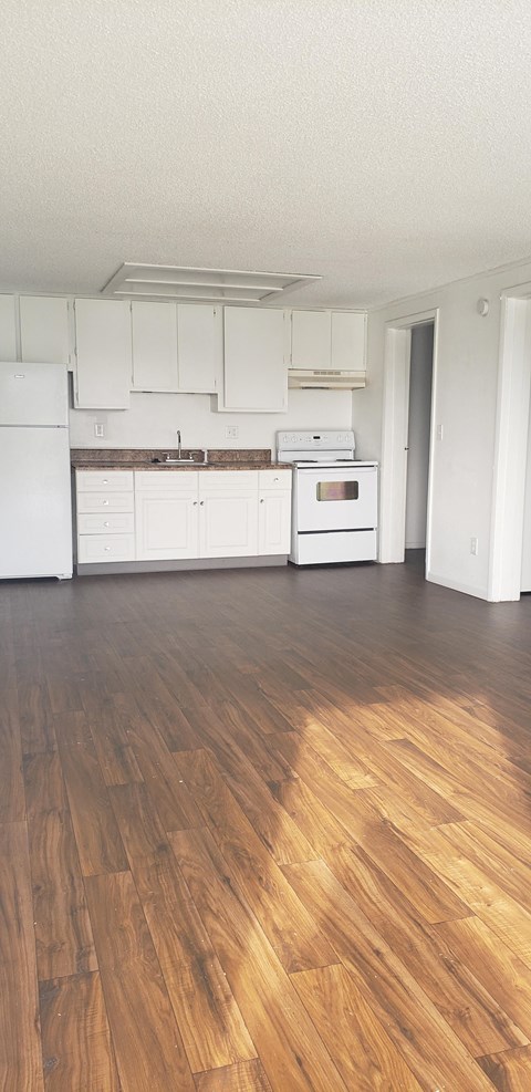an empty kitchen with white cabinets and a wooden floor