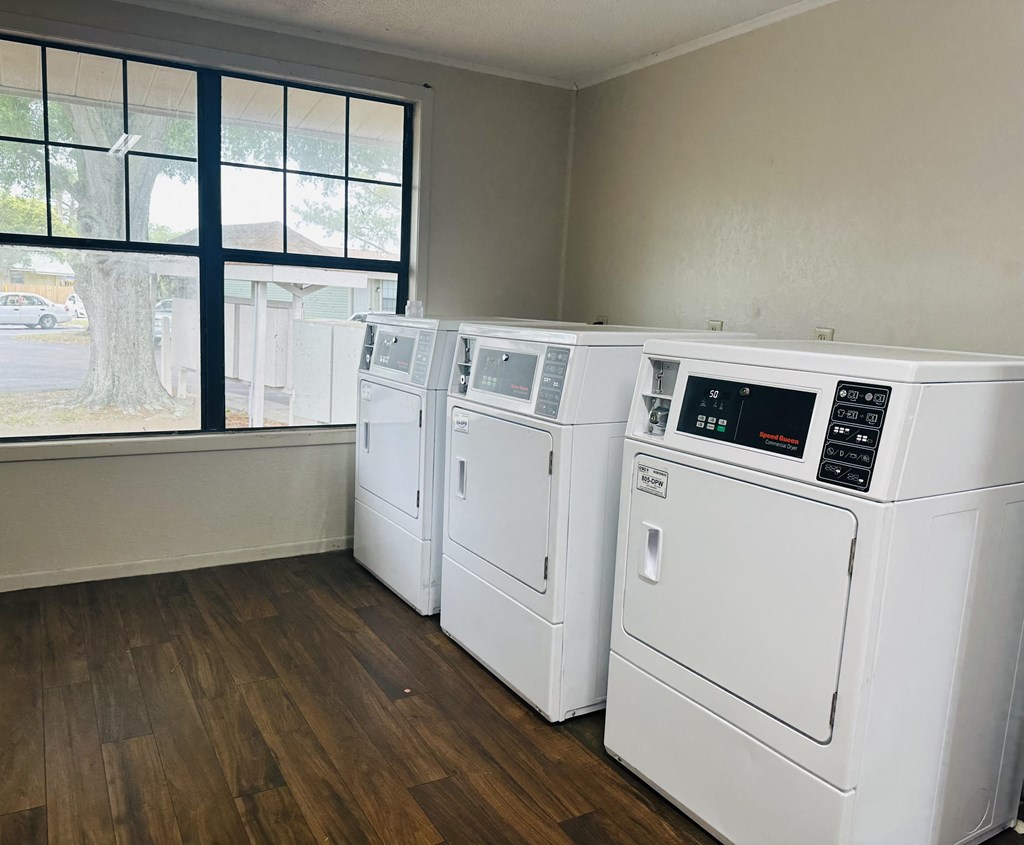 an empty laundry room with four washers and dryers and a window