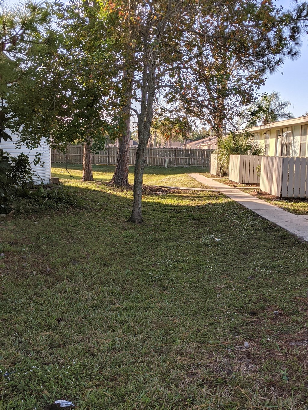 a yard with a fence and trees and a sidewalk