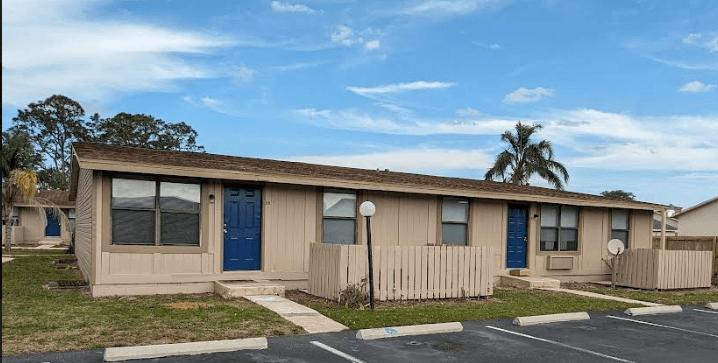 a small tan building with two blue doors and a fence