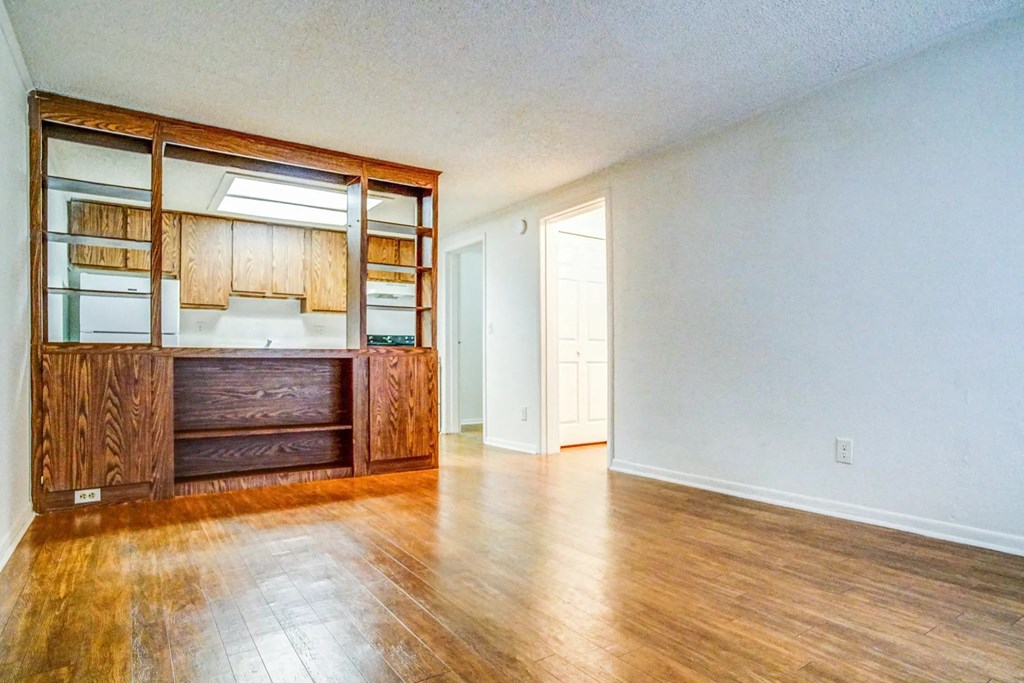 an empty living room with wood floors and a kitchen