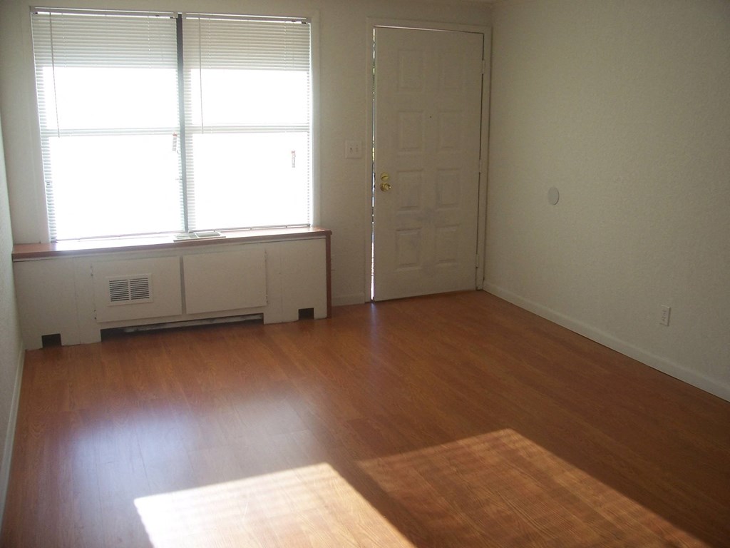 an empty living room with wooden floors and a door and window