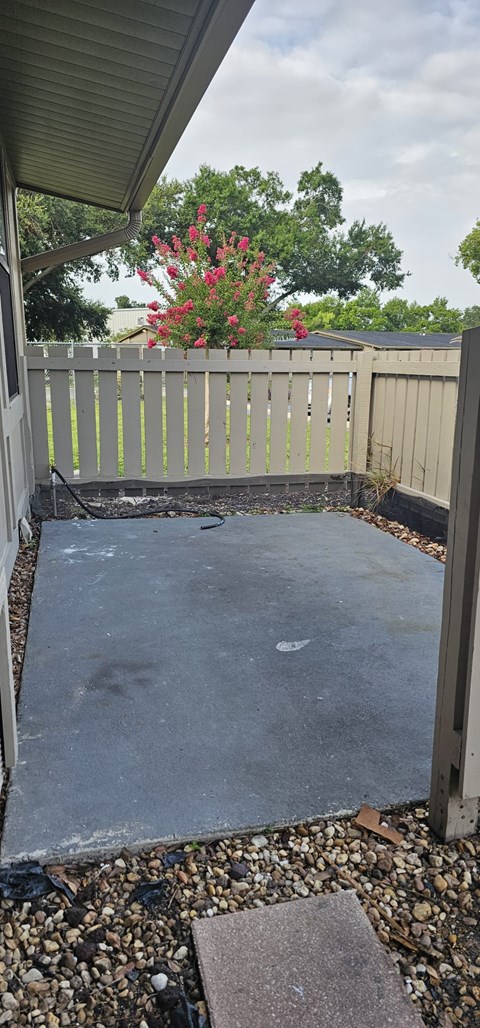 A concrete patio with a white fence and a red flowering bush in the background.