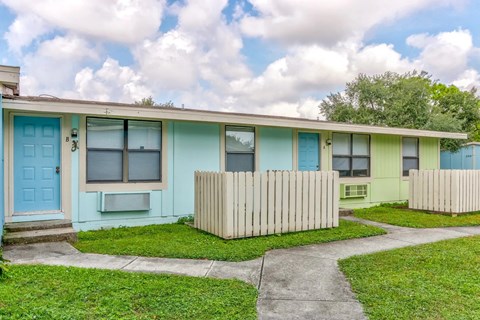 a blue and green house with a sidewalk and grass