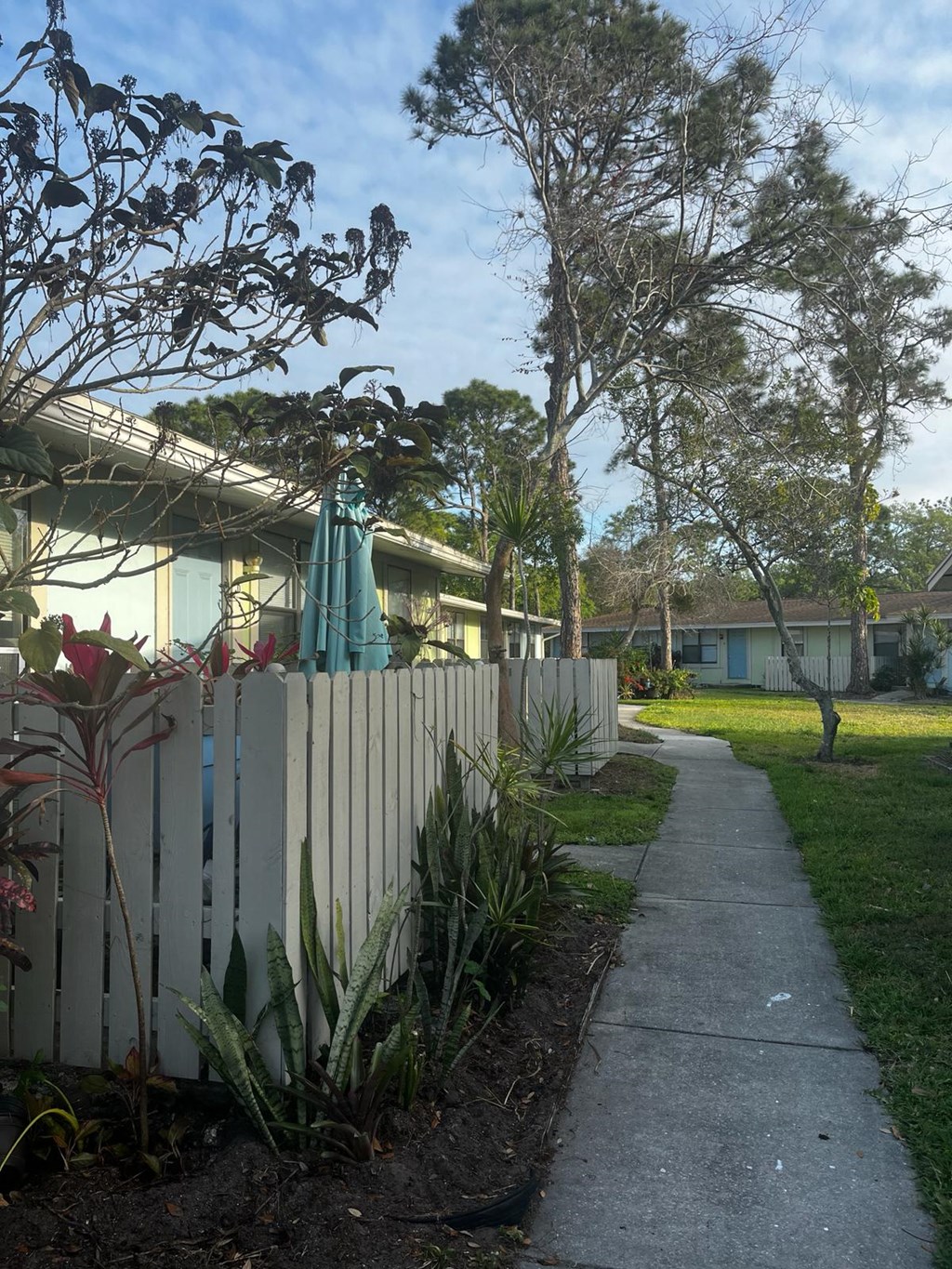 a sidewalk in front of a house with a white fence