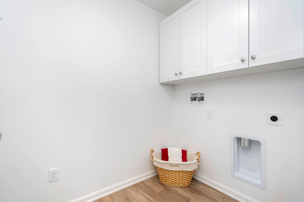 A laundry basket with a red and white striped cover sits on a wooden floor in a room with white walls and cabinets.