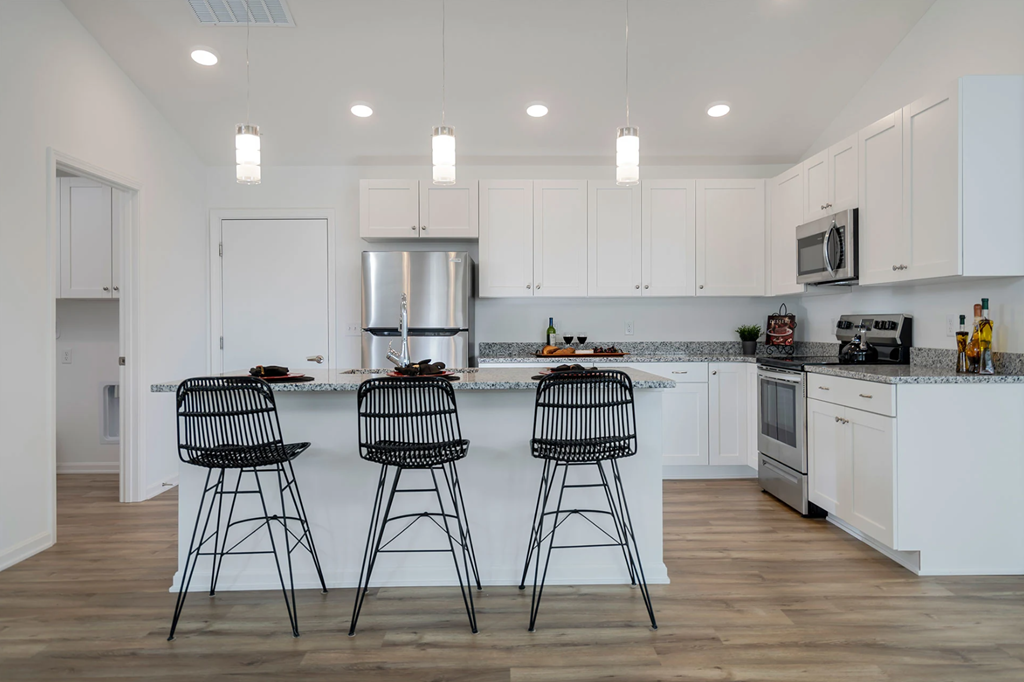 A kitchen with white cabinets and a bar area with two black chairs.