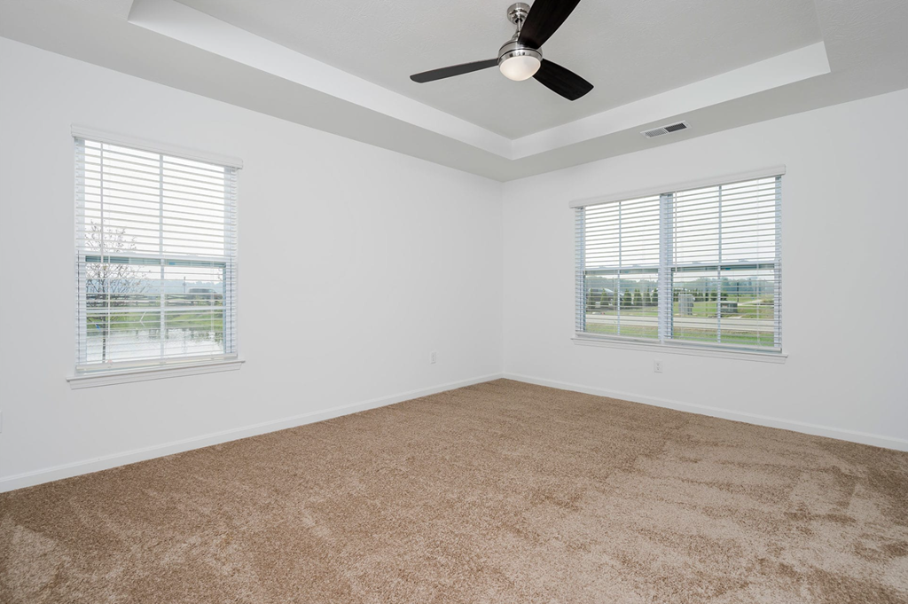 A room with a ceiling fan and two windows with blinds.