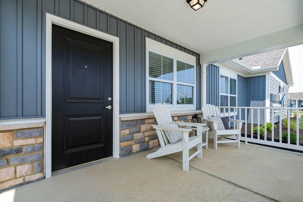 A black door is on the left of a porch with white chairs.
