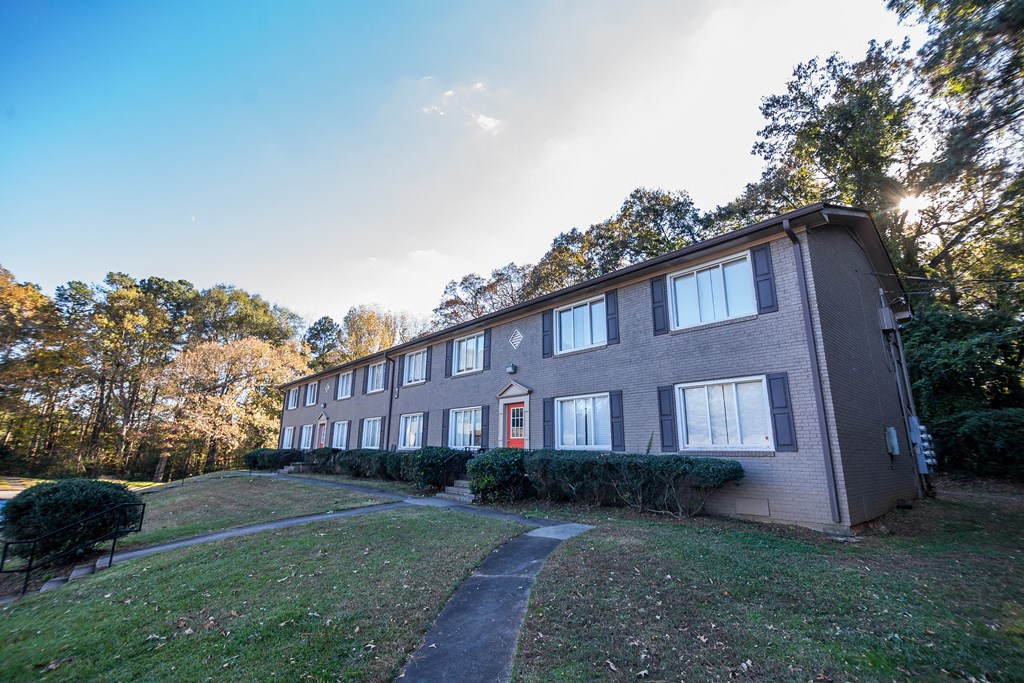 a brick building with a red door on a grassy hill with trees in the background at Broadway at East Atlanta, Atlanta, GA