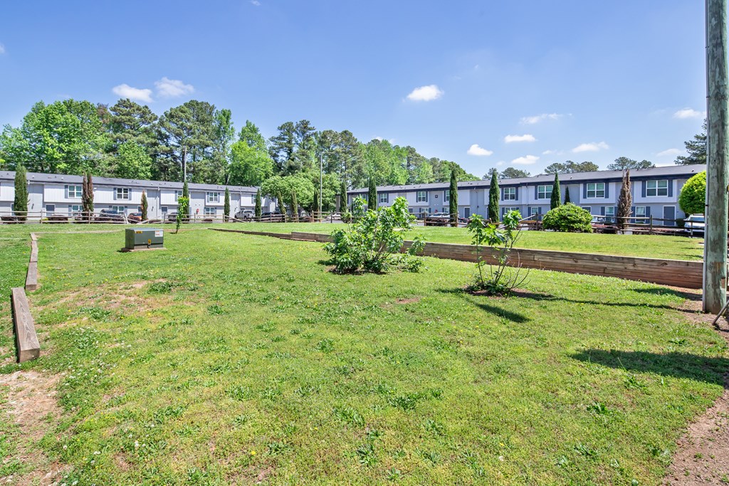 A grassy area with a wooden fence and a path leading to a row of houses.