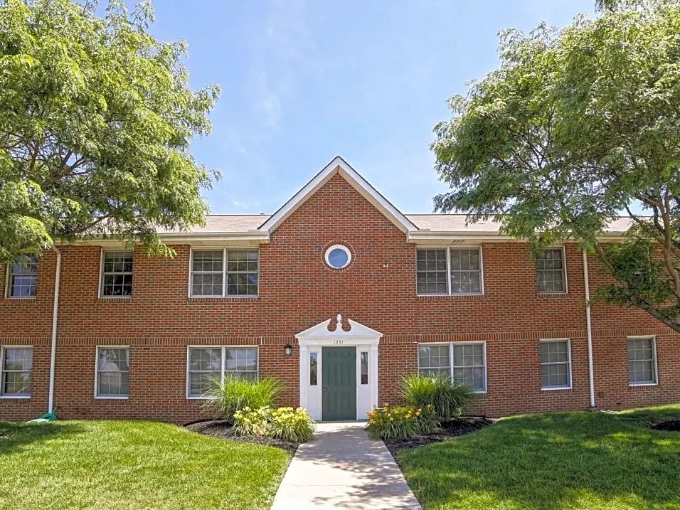 the front of a brick house with a green lawn and trees