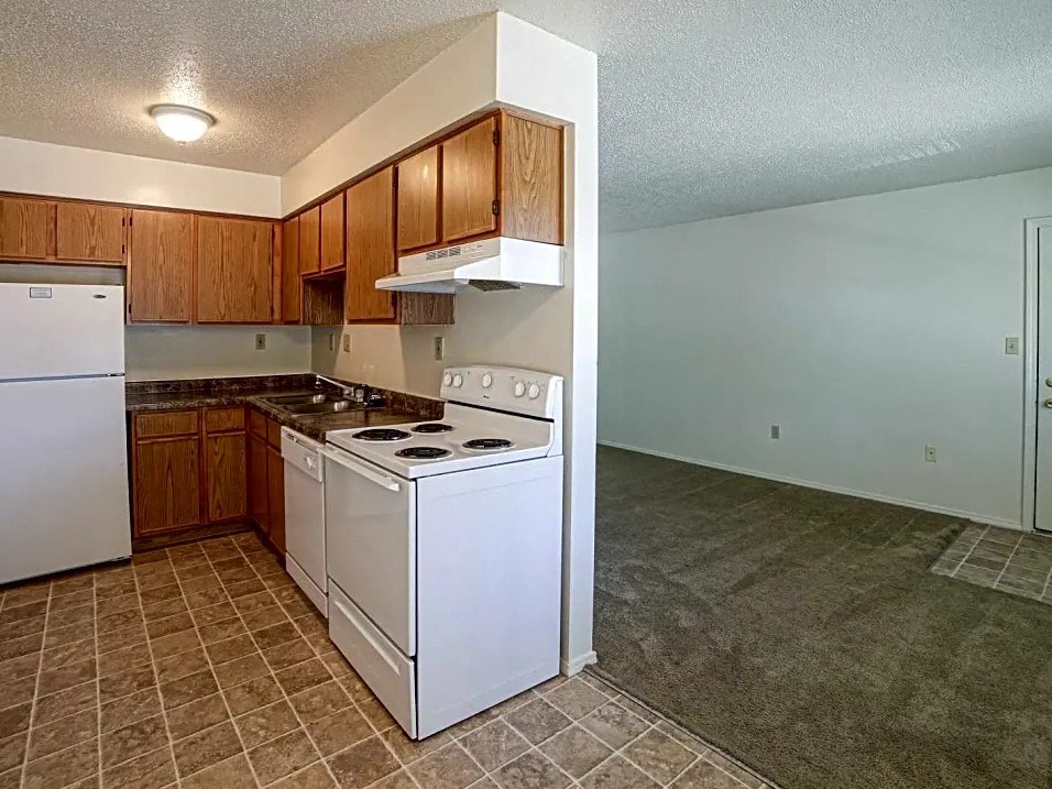 an empty kitchen with white appliances and wooden cabinets
