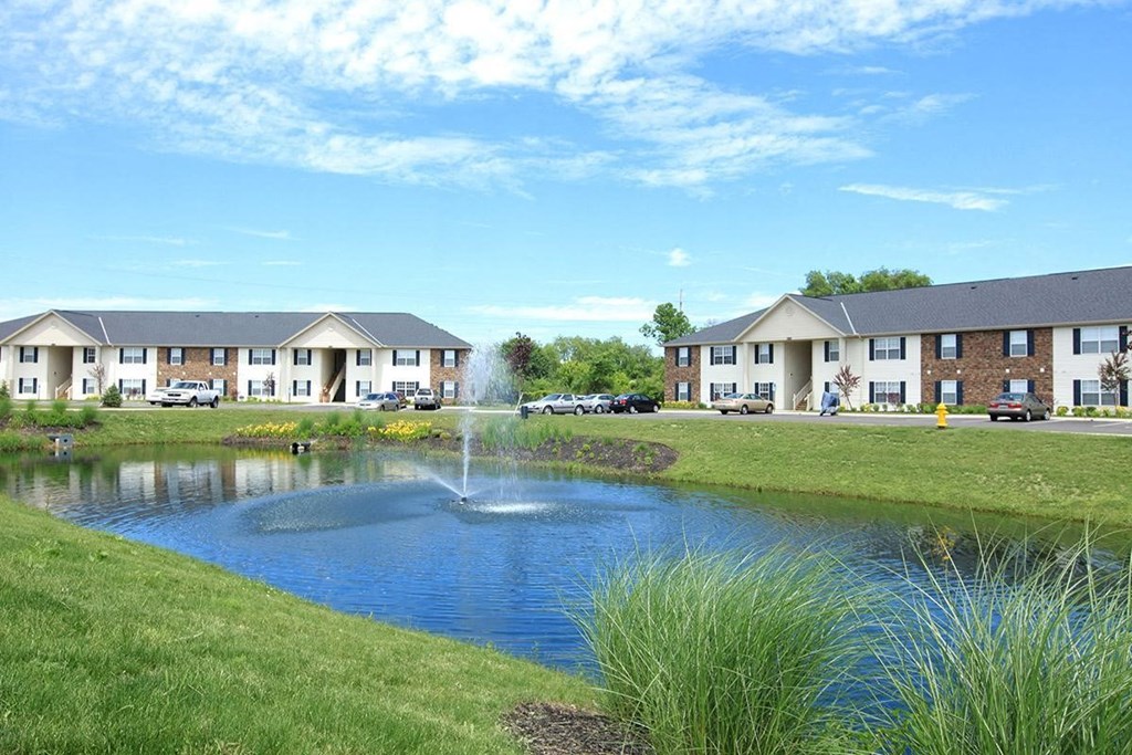 a pond with a fountain in the middle of a apartment complex
