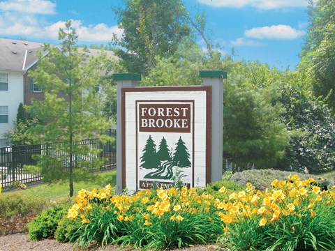 A sign for Forest Brooke Apartments is surrounded by yellow flowers.