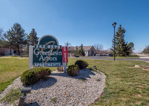 A sign for Greenlawn Arbors Apartments is displayed in front of a building.