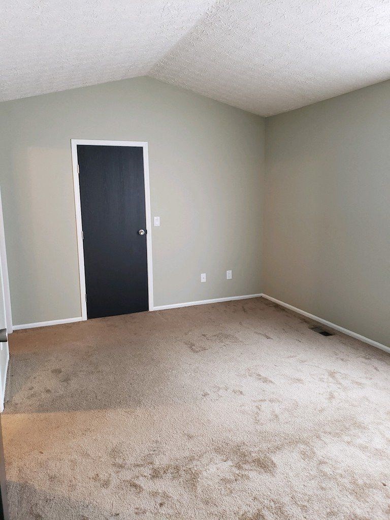 an empty room with a black door and a carpeted floor