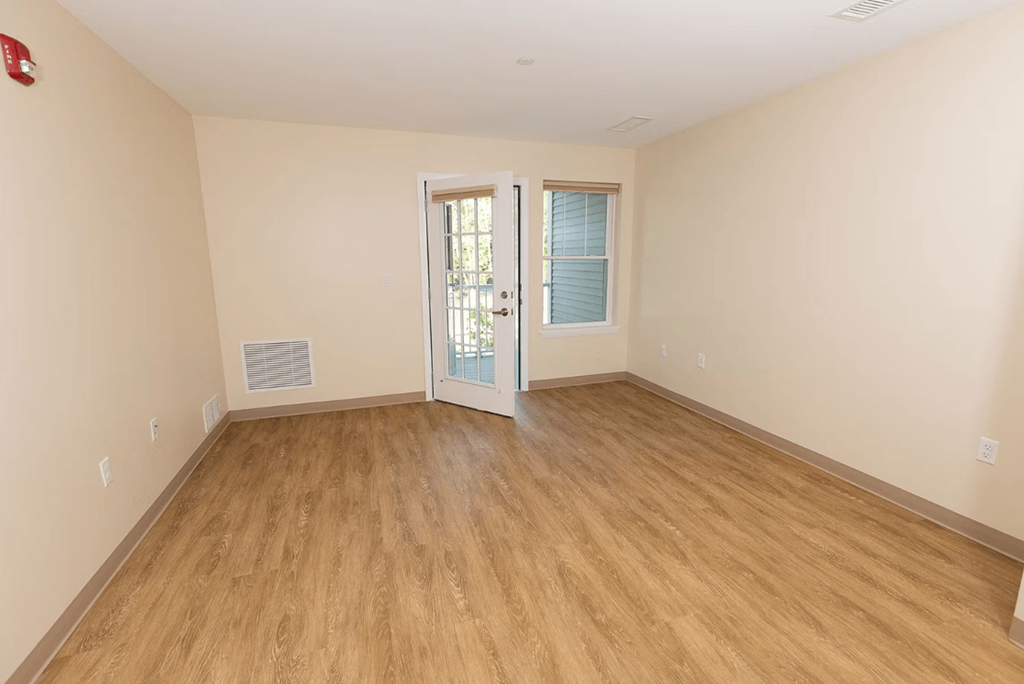 A room with wooden flooring and a door leading to another room.