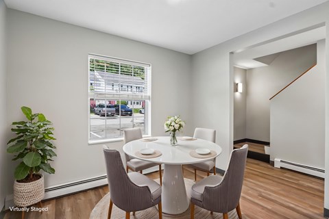 A dining room with a table set for four and a view of a parking lot outside the window.