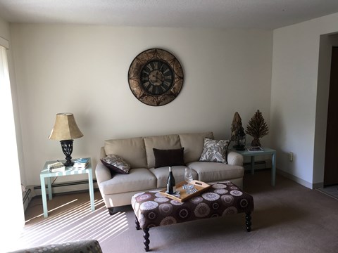 A living room with a couch, a table with a lamp, and a clock on the wall.