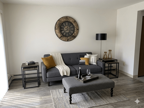 A living room with a grey couch, a coffee table, and a large clock on the wall.