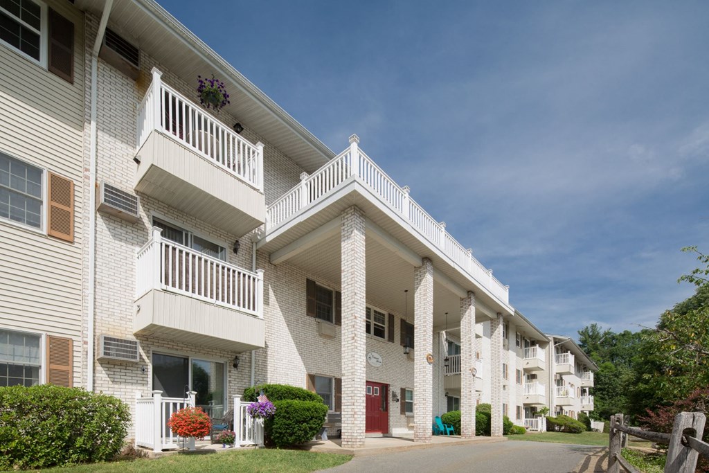 A white apartment building with balconies and a red door.