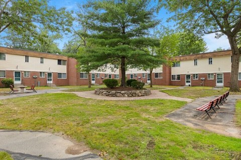 A grassy area with benches and trees in front of apartment buildings.