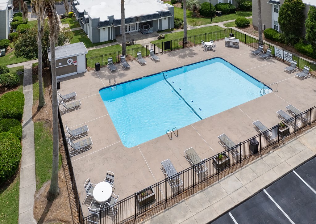 A large swimming pool surrounded by lounge chairs and a fence.