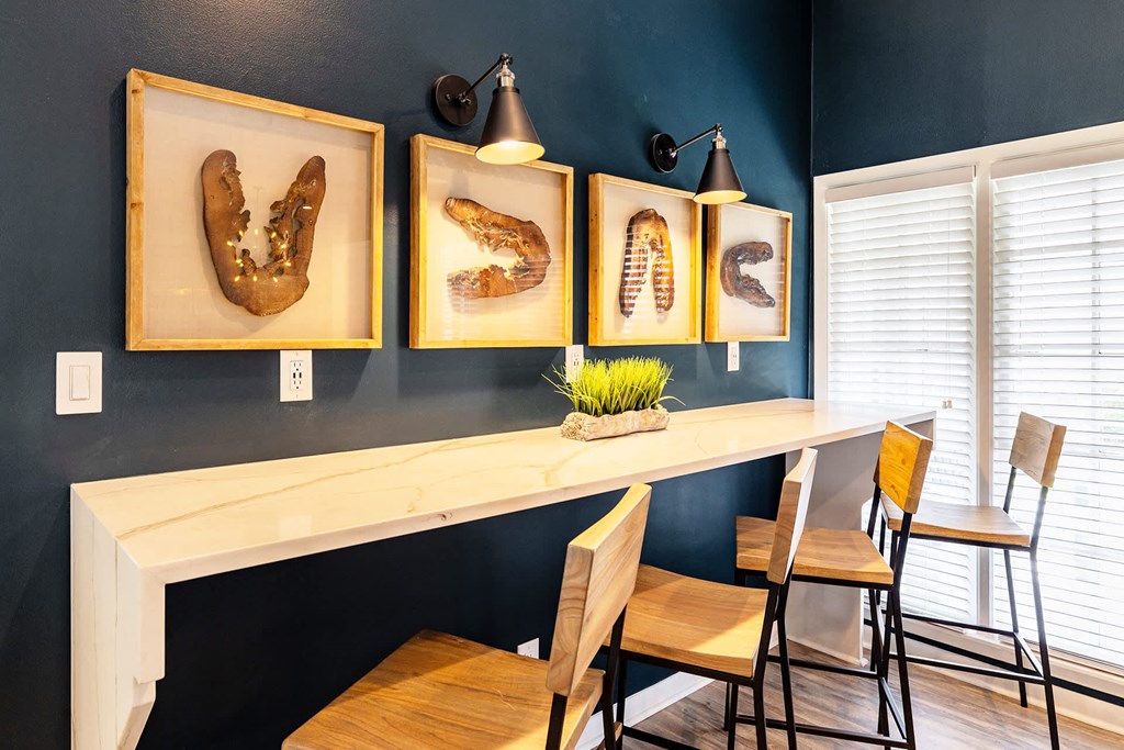 A white desk with a plant and three framed objects on a blue wall.