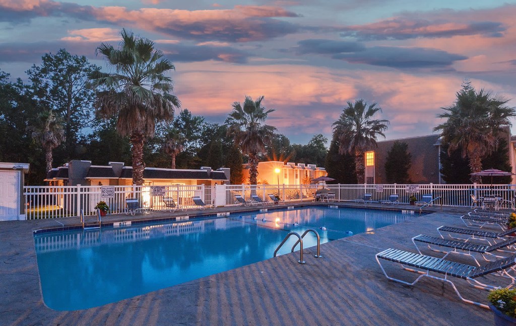 A pool surrounded by palm trees and lounge chairs.
